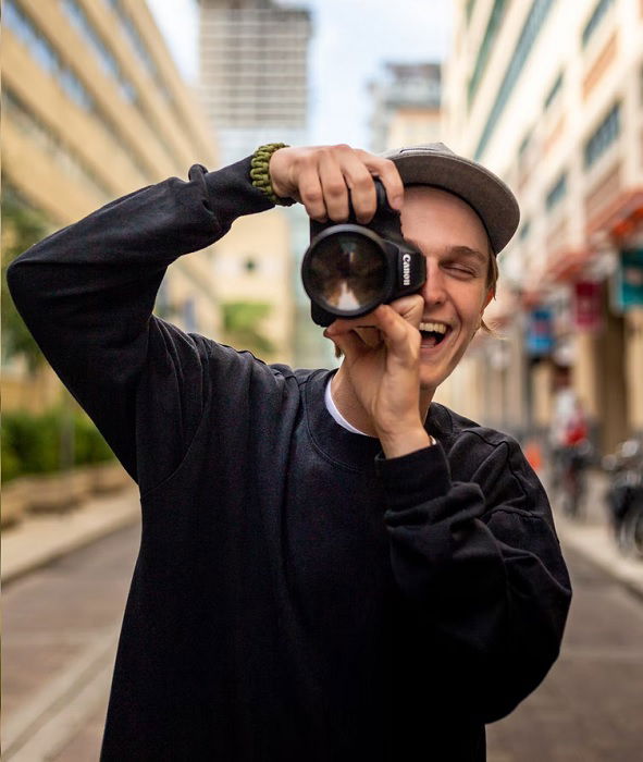 Young man in cap holding a canon camera to his face.