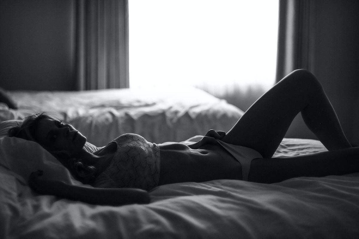 Black-and-white photo of woman lying in bed in lingerie as an example of backlight for DIY boudoir photos