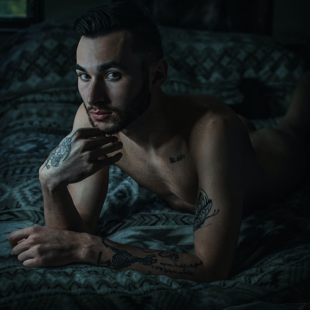 A male with tatoos posing in bed as an example for DIY boudoir photos