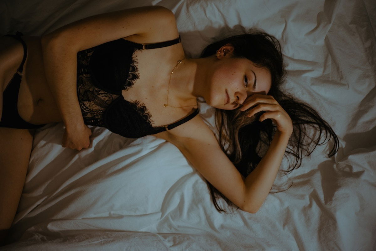 Overhead shot of a woman posing in lingerie in bed as an example for simple white sheets for DIY boudoir photos