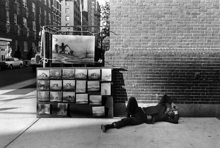 Man sleeps on street next to art stall