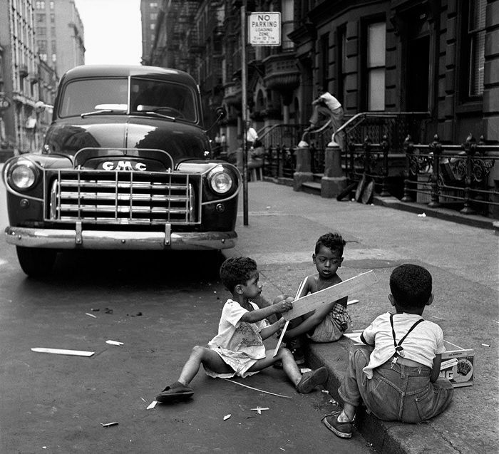 Three kids sitting in the street in front of a care