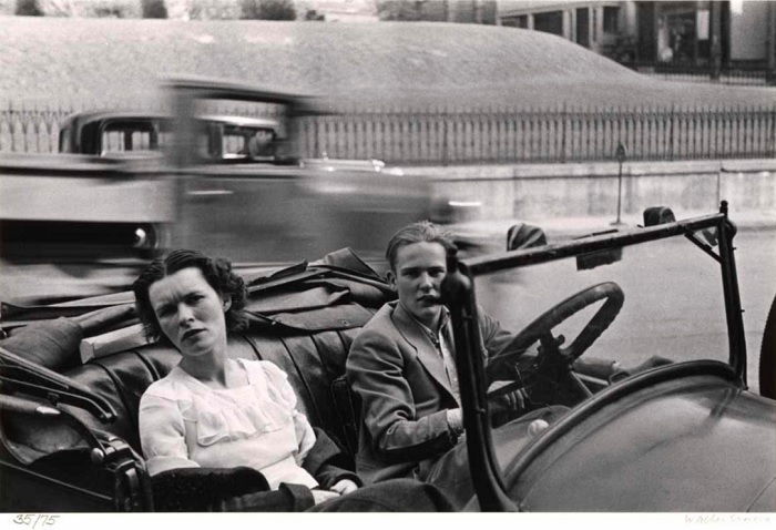 Two women in a stationary car as others pass by