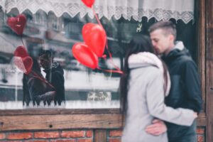 Couple embracing outside with heart balloons and reflection in a window as a Valentines day photoshoot idea