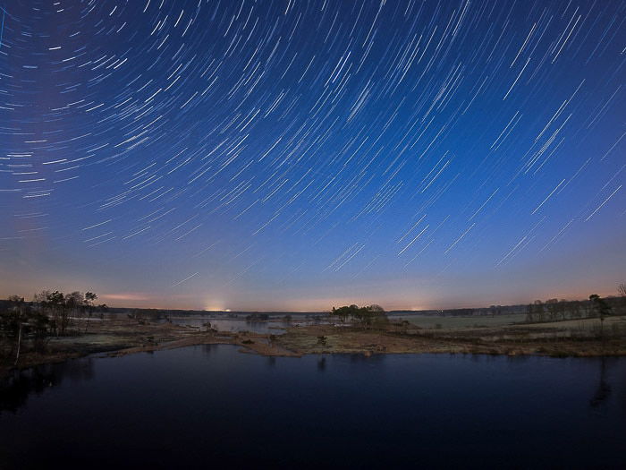 Nocturnal landscape over water and star trails above for creative motion blur