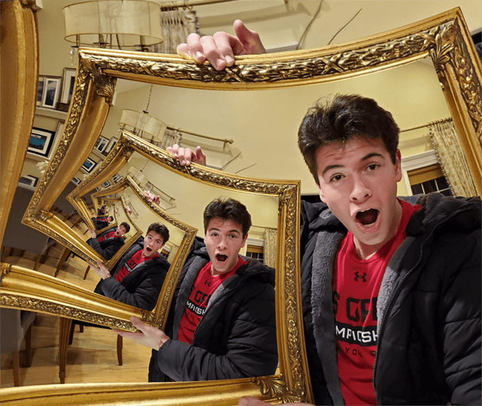 A man taking a selfie in a gallery using a triptych of mirrors.